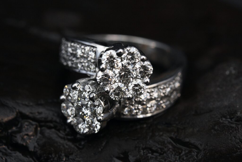 Close-up of two silver rings with cluster-set diamonds and pavé diamond bands on a dark surface.