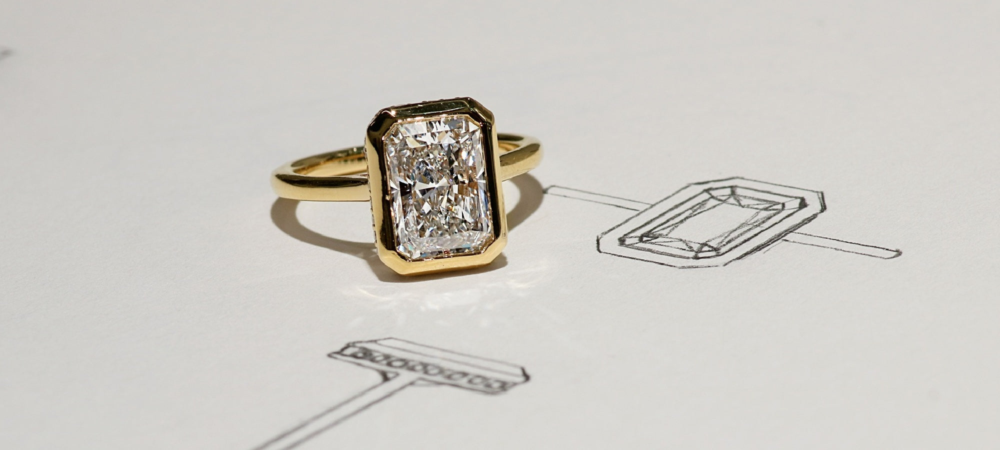 Gold ring with a rectangular radiant-cut diamond on a sketch of its design.