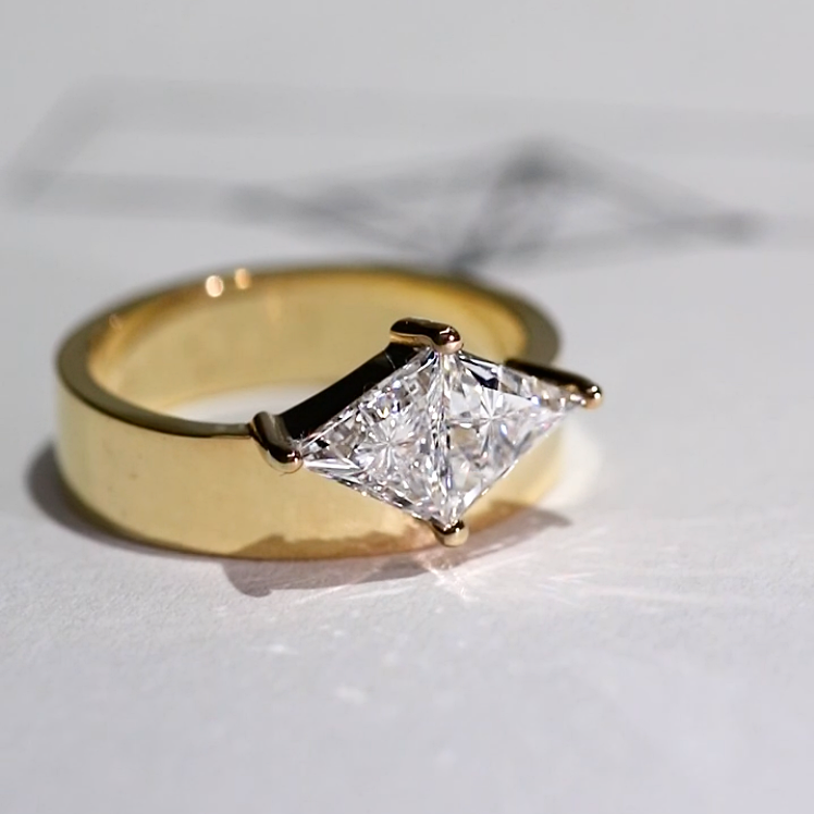 Gold ring with a wide band featuring a central geometric diamond set in a unique angular design.