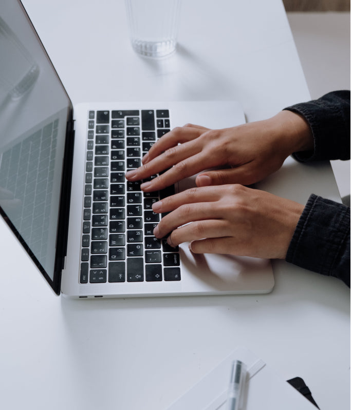 Hands typing on a silver laptop with a black keyboard on a white desk.