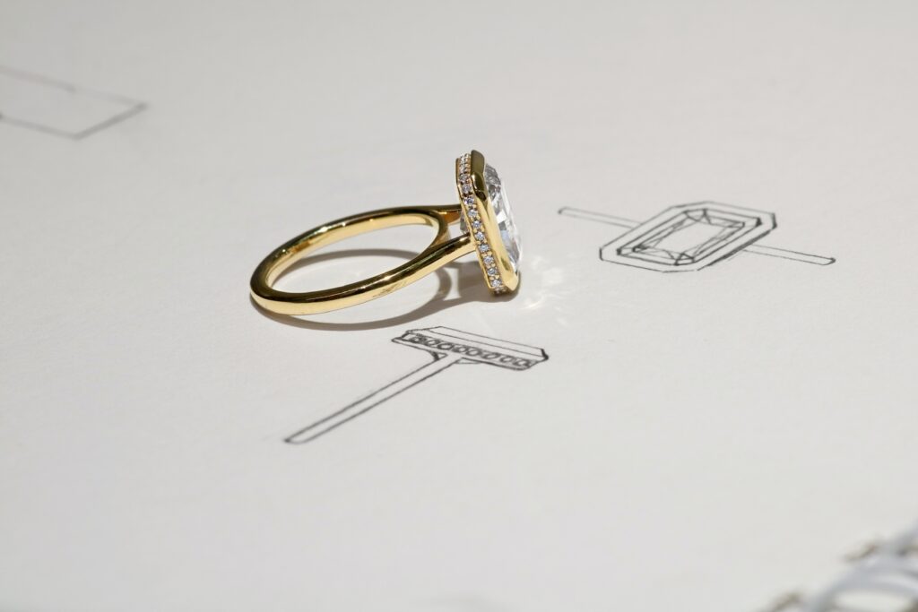 Gold engagement ring with a large rectangular diamond on a paper with ring design sketches.