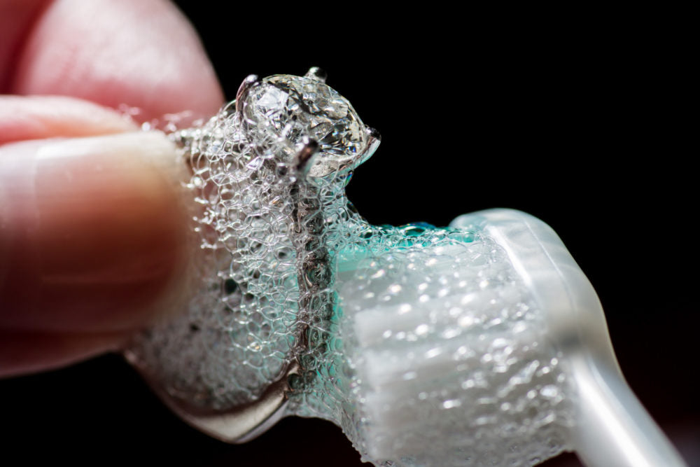 Cleaning diamond engagement ring with toothbrush and soap.