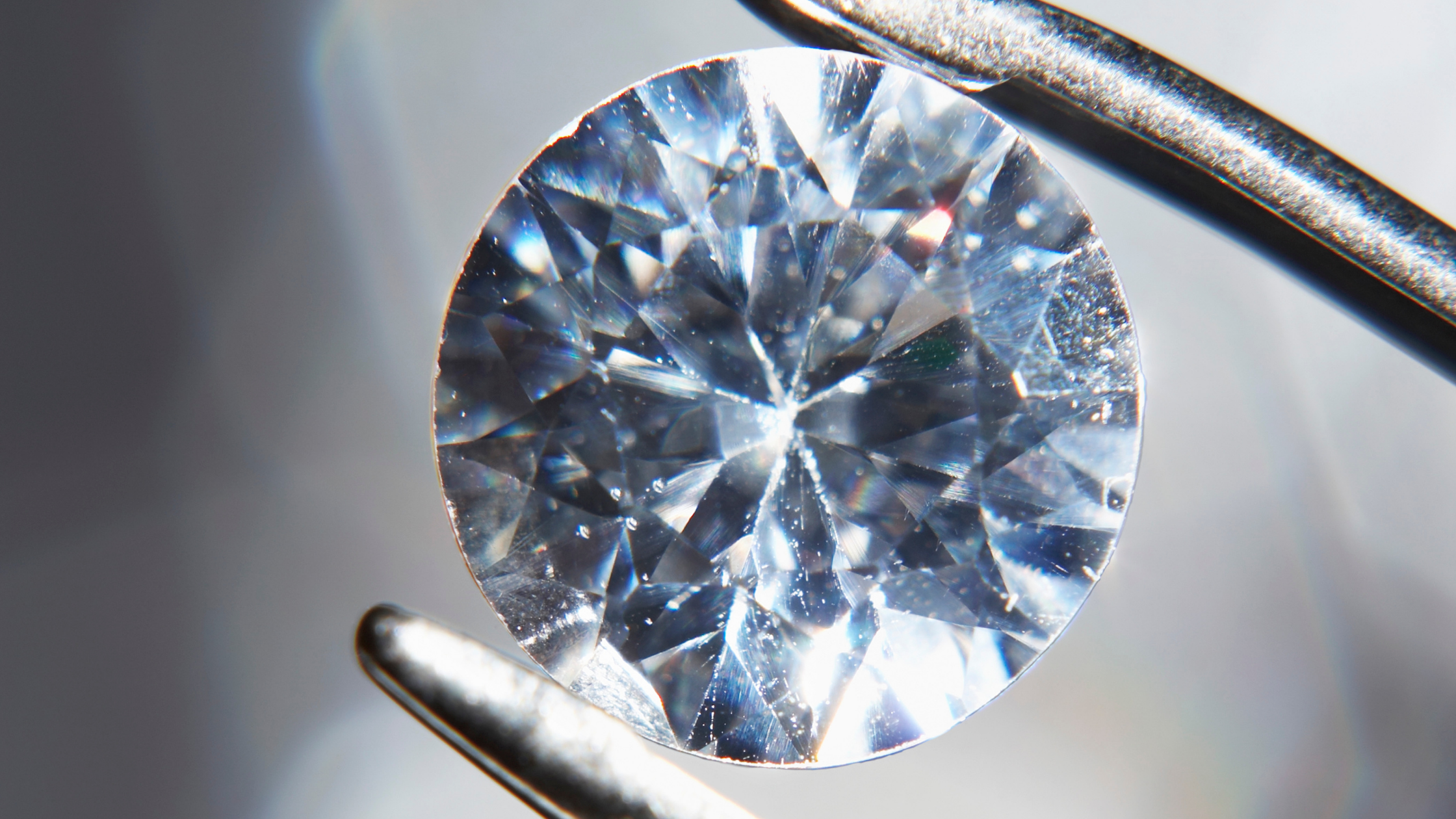 Close-up of round cut diamond held by tweezers.