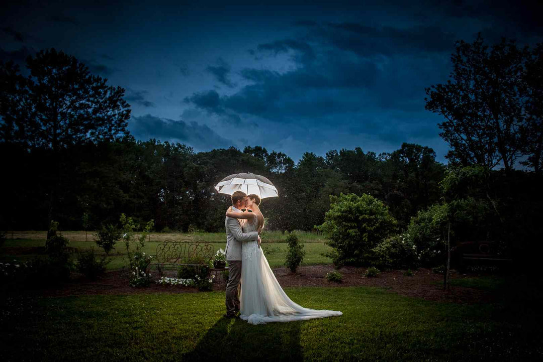 Newlyweds kissing under an umbrella in the rain.