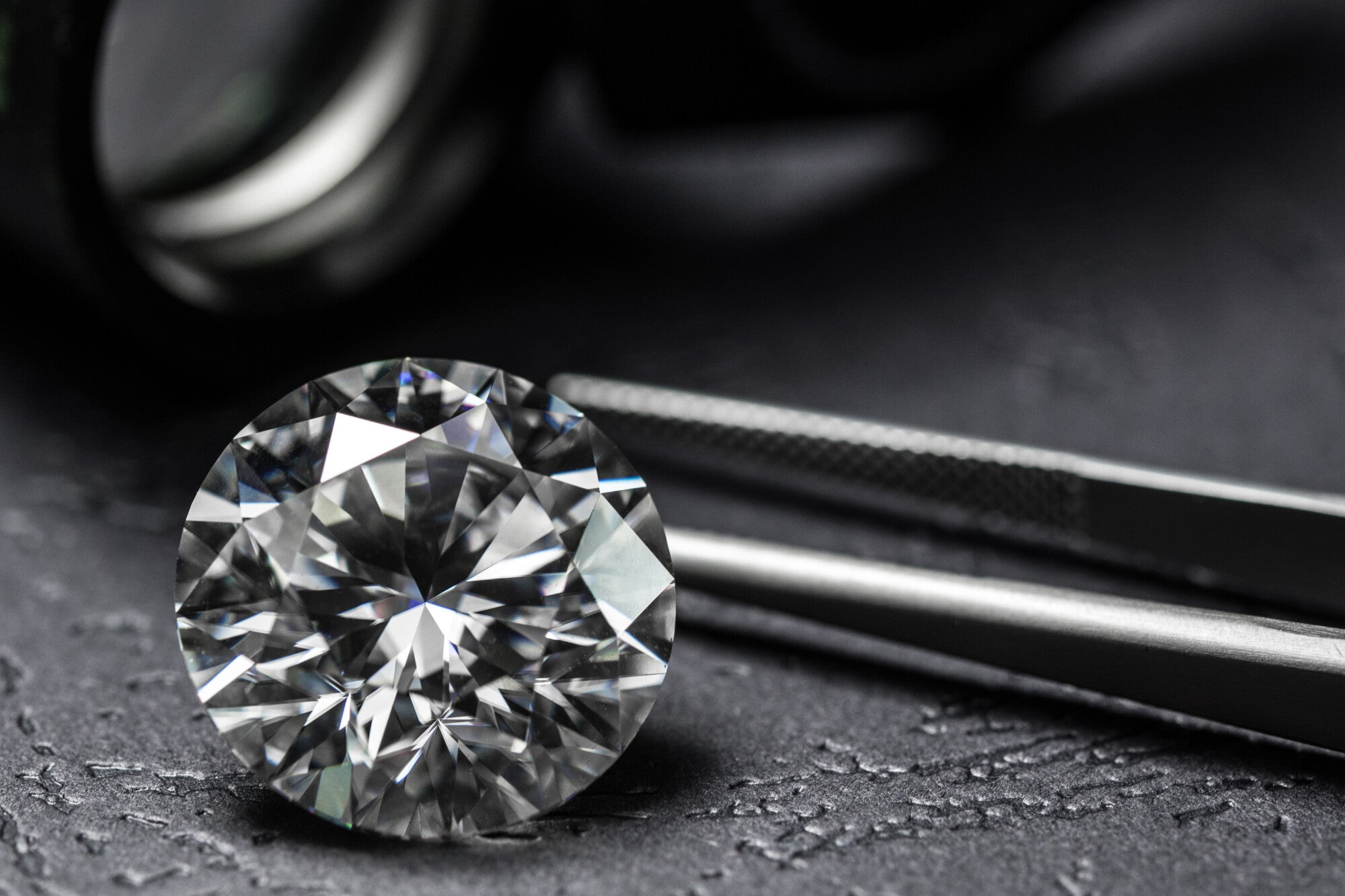 Lab-created round cut diamond with tweezers.