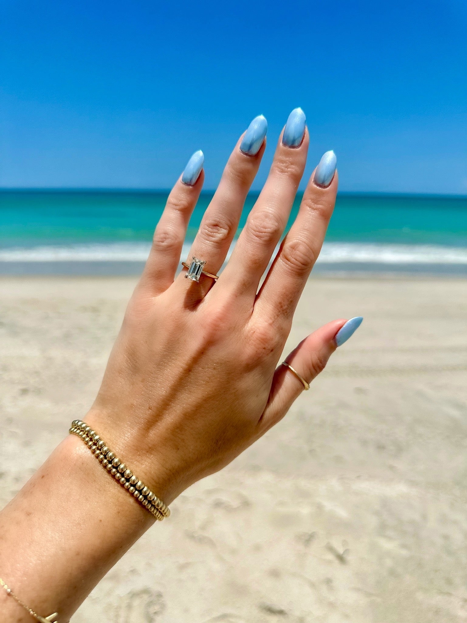 Masina Diamonds Emerald Cut engagement ring on the beach.