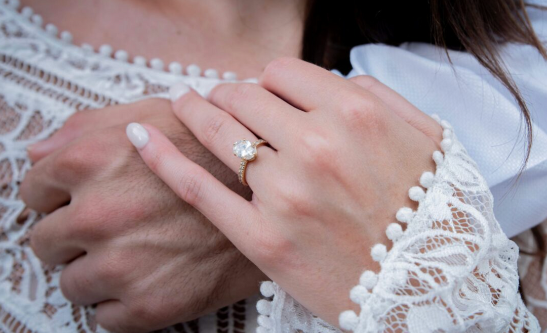 Couple holding hands, featuring a gold diamond engagement ring.