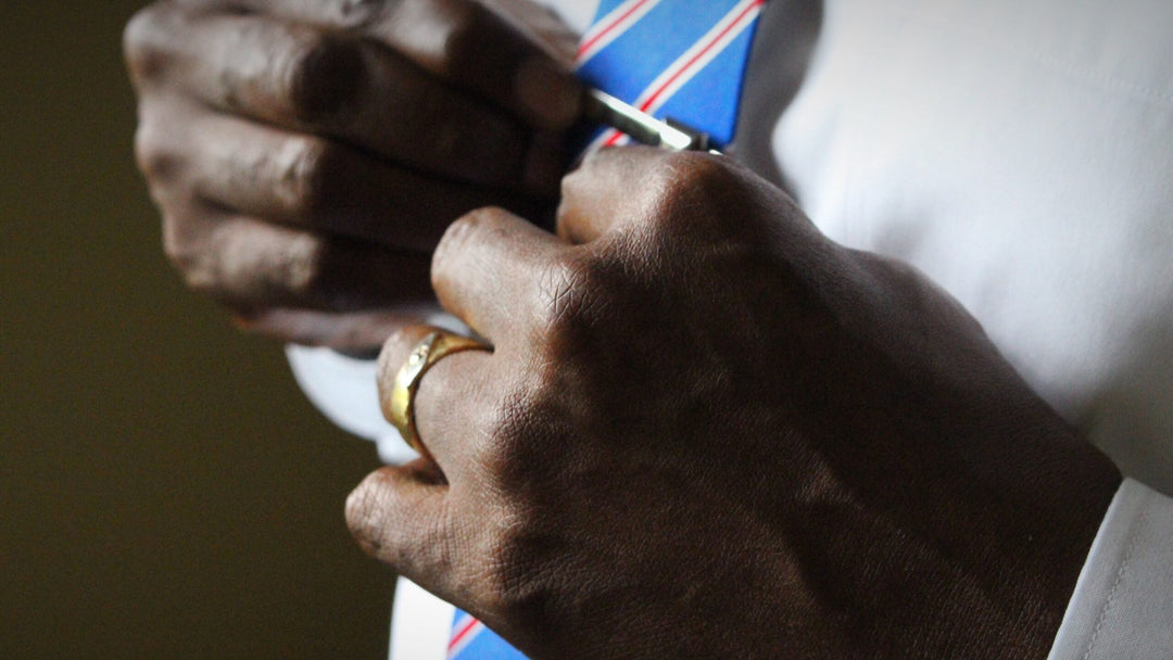Man adjusts tie, wearing gold diamond wedding band.