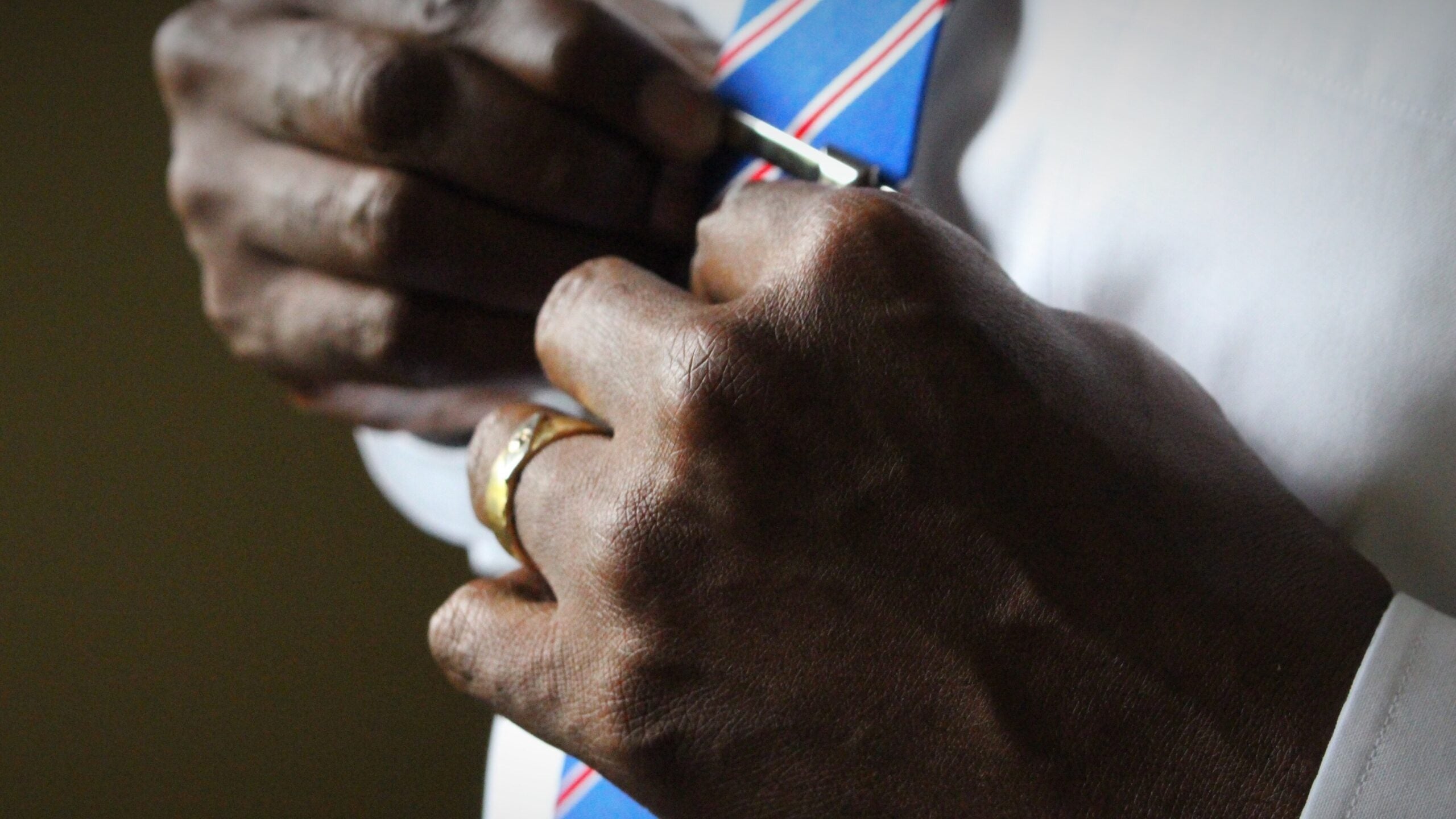 Man adjusts tie, wearing gold diamond wedding band.