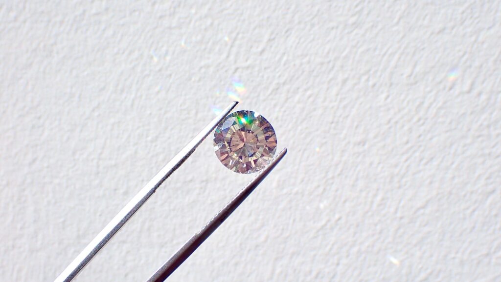 Round cut diamond held by tweezers.