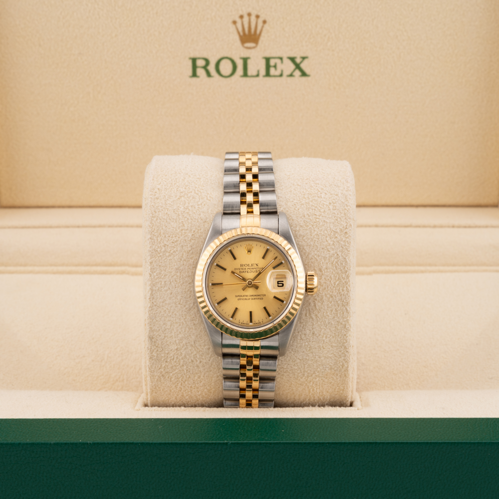 Rolex watch with gold and silver band on a cushion with Rolex logo in the background