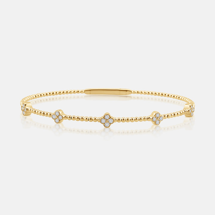 A delicate gold bangle bracelet featuring five small floral motifs set with clear stones, displayed on a clean white background with a soft reflection.