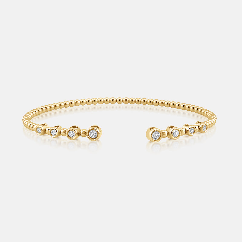 A gold beaded cuff bracelet with three bezel-set round diamond accents on each end, displayed on a clean light gray background.