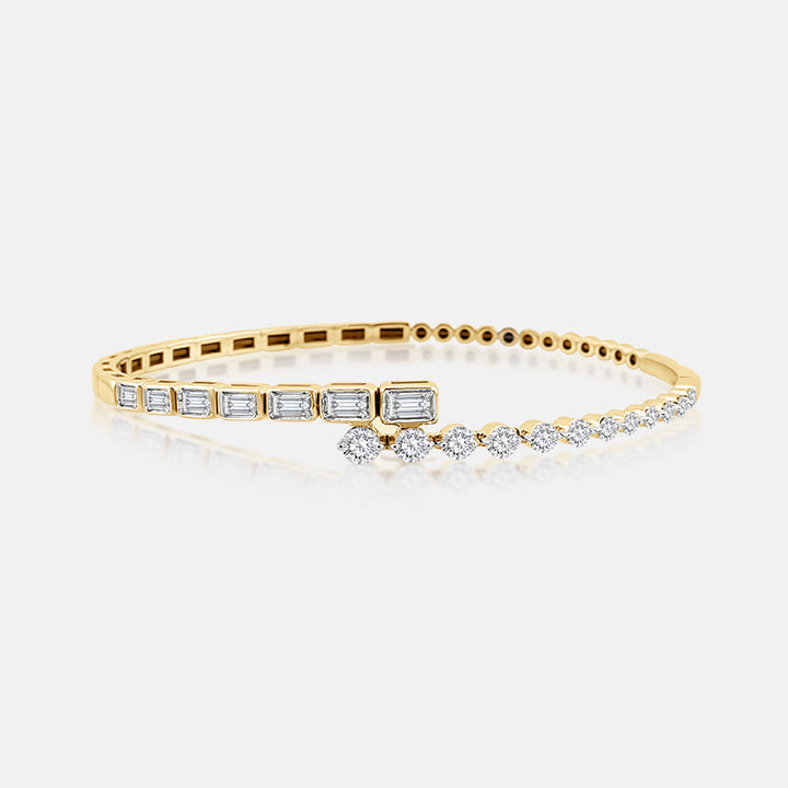 A yellow gold hinged bangle bracelet featuring baguette-cut and round-cut clear stones, displayed on a clean light gray background.