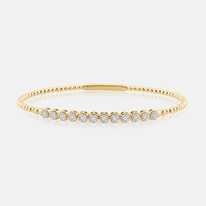 A delicate yellow gold tennis bracelet with a beaded chain and a row of round-cut clear gemstones, displayed on a light gray background.