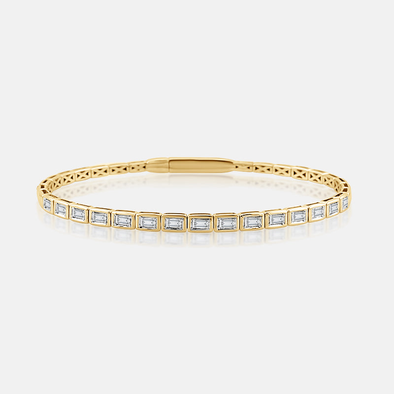 A yellow gold bezel set bracelet featuring emerald cut diamonds, displayed on a clean light gray background with a soft reflection.