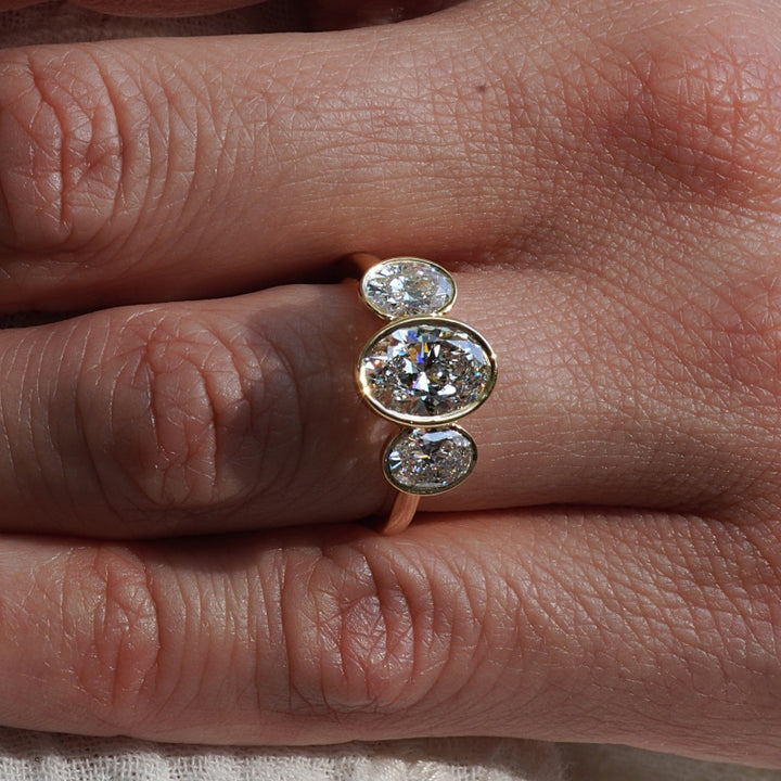 A close-up of a gold ring with three vertically aligned oval-cut clear gemstones worn on a person's finger.