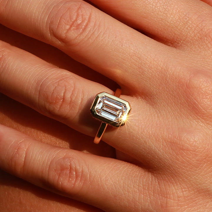emerald cut bezel set engagement ring on a woman's hand