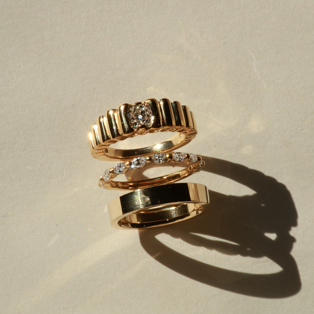 Three gold rings with diamond accents on a beige background