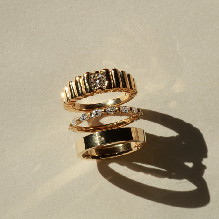 Three gold rings with diamond accents on a beige background
