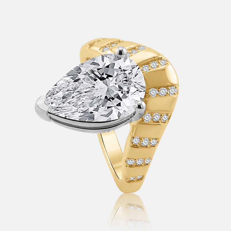 A pear-cut diamond ring set in a contour yellow gold cloud style band with small accent diamonds, shown on a light gray background with a soft reflection.