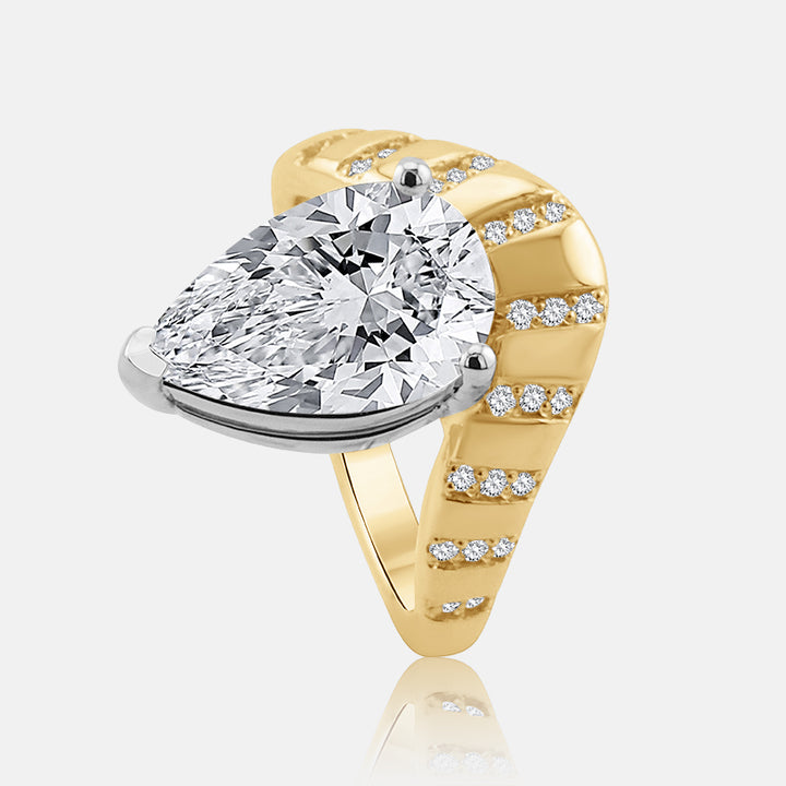 A pear-cut diamond ring set in a contour yellow gold cloud style band with small accent diamonds, shown on a light gray background with a soft reflection.