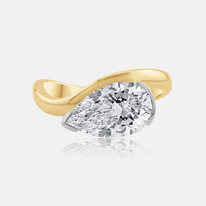 A yellow gold ring featuring a large, brilliant-cut pear-shaped diamond in a prong setting, shown on a light gray background with a soft reflection below.