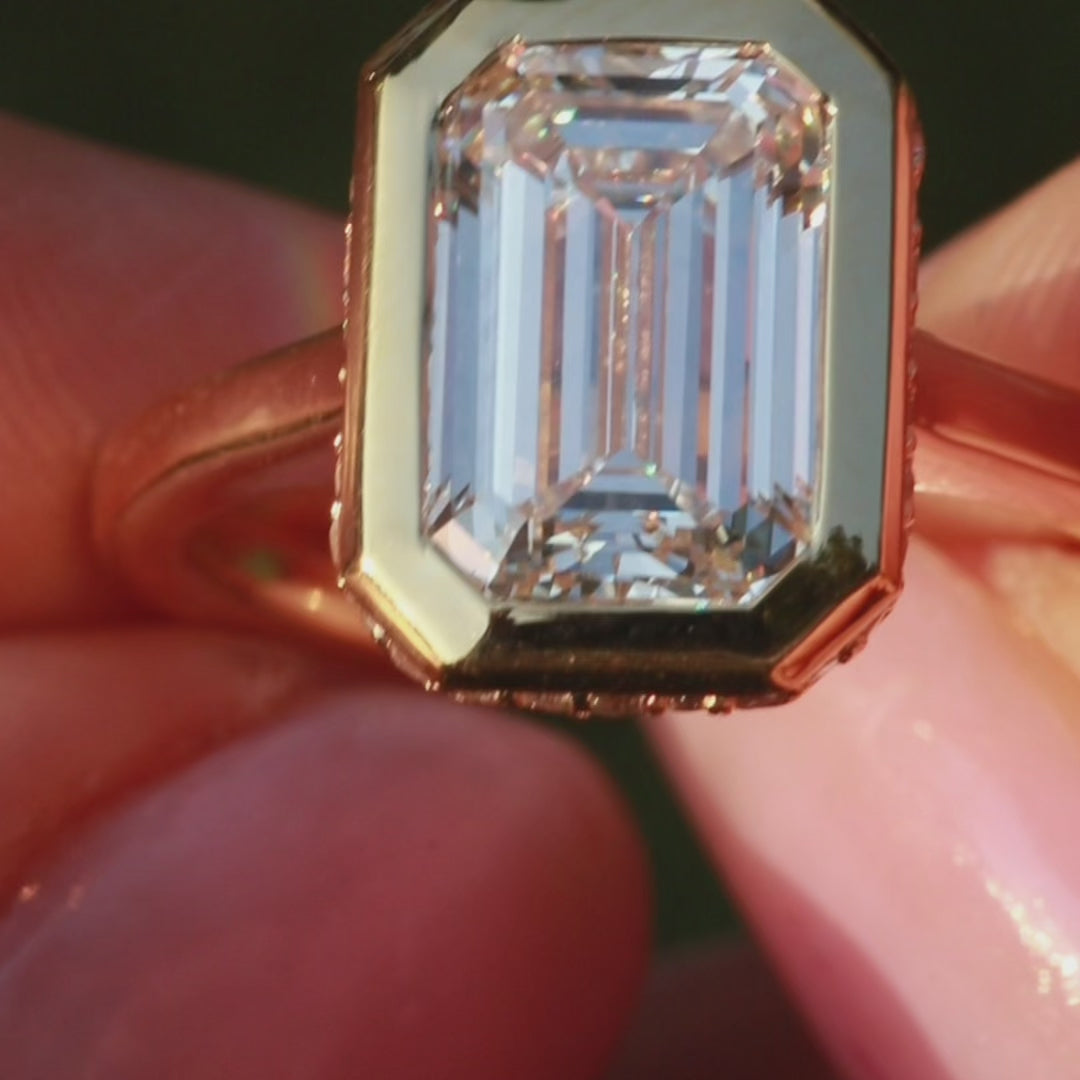 bezel set engagement ring with emerald cut diamond center stone and hidden halo in yellow gold